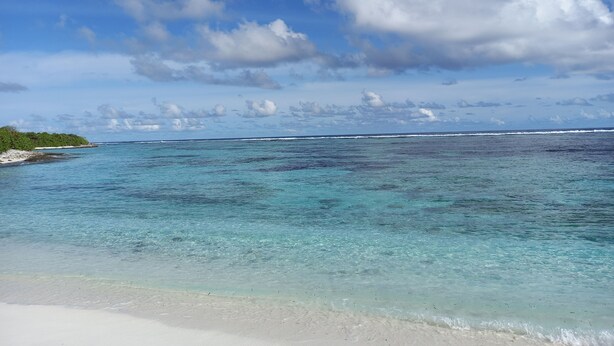 A beach with clear turquoise waters, white sand, and a distant shoreline with vegetation. - IRUKA GUESTHOUSE (Fiyoaree)