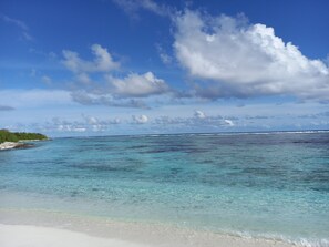 A beach with clear turquoise waters, white sand, and a distant shoreline with vegetation. - IRUKA GUESTHOUSE (Fiyoaree)