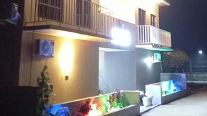 A multi-story building with balconies, an air conditioning unit, and a well-lit exterior. - IRUKA GUESTHOUSE (Fiyoaree)