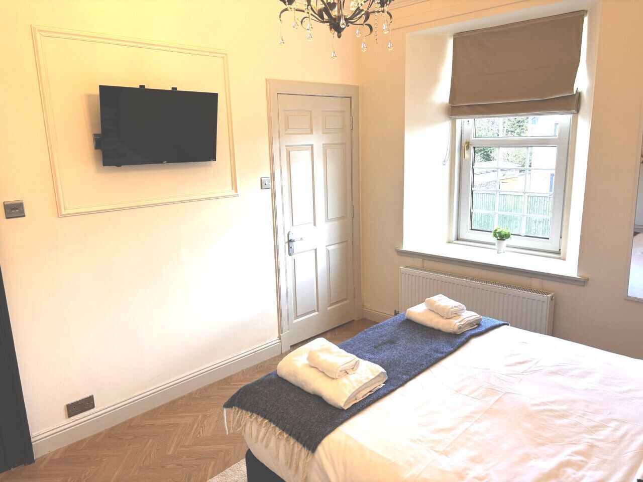A hotel room with a bed, a television mounted on the wall, a door, and a window with a view of the outside.