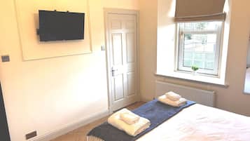 A hotel room with a bed, a television mounted on the wall, a door, and a window with a view of the outside.