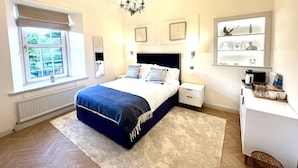 Een slaapkamer met een groot bed, nachtkastjes, een kroonluchter, een raam met jaloezieën en een bureau met een stoel.