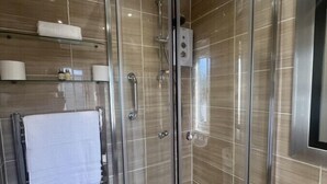 Een moderne douchecabine met een glazen deur, een handdoekhouder met een witte handdoek, en een toiletrolhouder aan de muur.