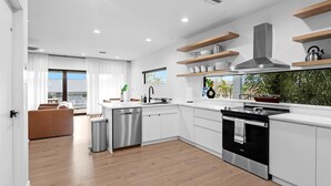 A modern kitchen with white cabinets, stainless steel appliances, and wooden shelves. - NEW 4 bd 3 bth, heated pool, golf cart block from beach (Indian Rocks Beach)
