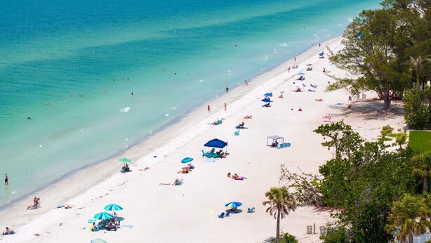 A beach with clear turquoise water, people sunbathing, and umbrellas. - NEW 4 bd 3 bth, heated pool, golf cart block from beach (Indian Rocks Beach)