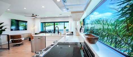 Una cucina moderna con una grande isola, elettrodomestici integrati e vista sul verde attraverso ampie finestre.
