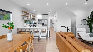 A modern kitchen with white cabinets, a central island, and a dining area with a wooden table and chairs. - NEW 4 bd 3 bth, heated pool, golf cart block from beach (Indian Rocks Beach)