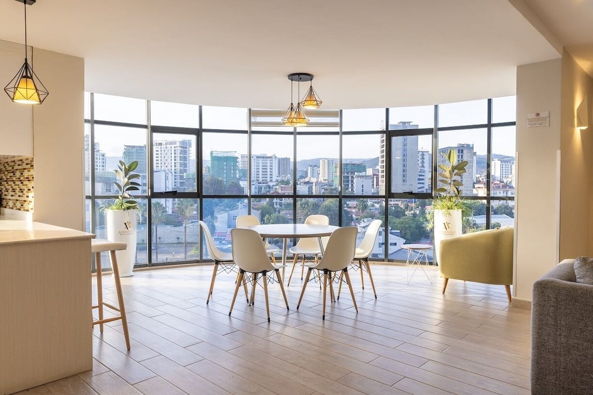 A modern dining area with a view of the cityscape through large windows, a round table, and contemporary chairs.