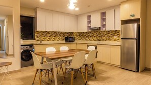 Una cucina moderna con un tavolo da pranzo in legno, sedie bianche, un frigorifero in acciaio inossidabile e una lavatrice.
