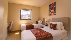 Camera d'albergo con due letti, una scrivania, una sedia, una finestra con vista sulla città e un quadro appeso al muro.