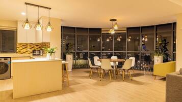 Una cocina moderna con una isla central, zona de comedor con sillas y ventanas amplias con vistas a la ciudad.