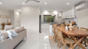 A modern kitchen with white cabinets, a wooden dining table, and a ceiling fan.