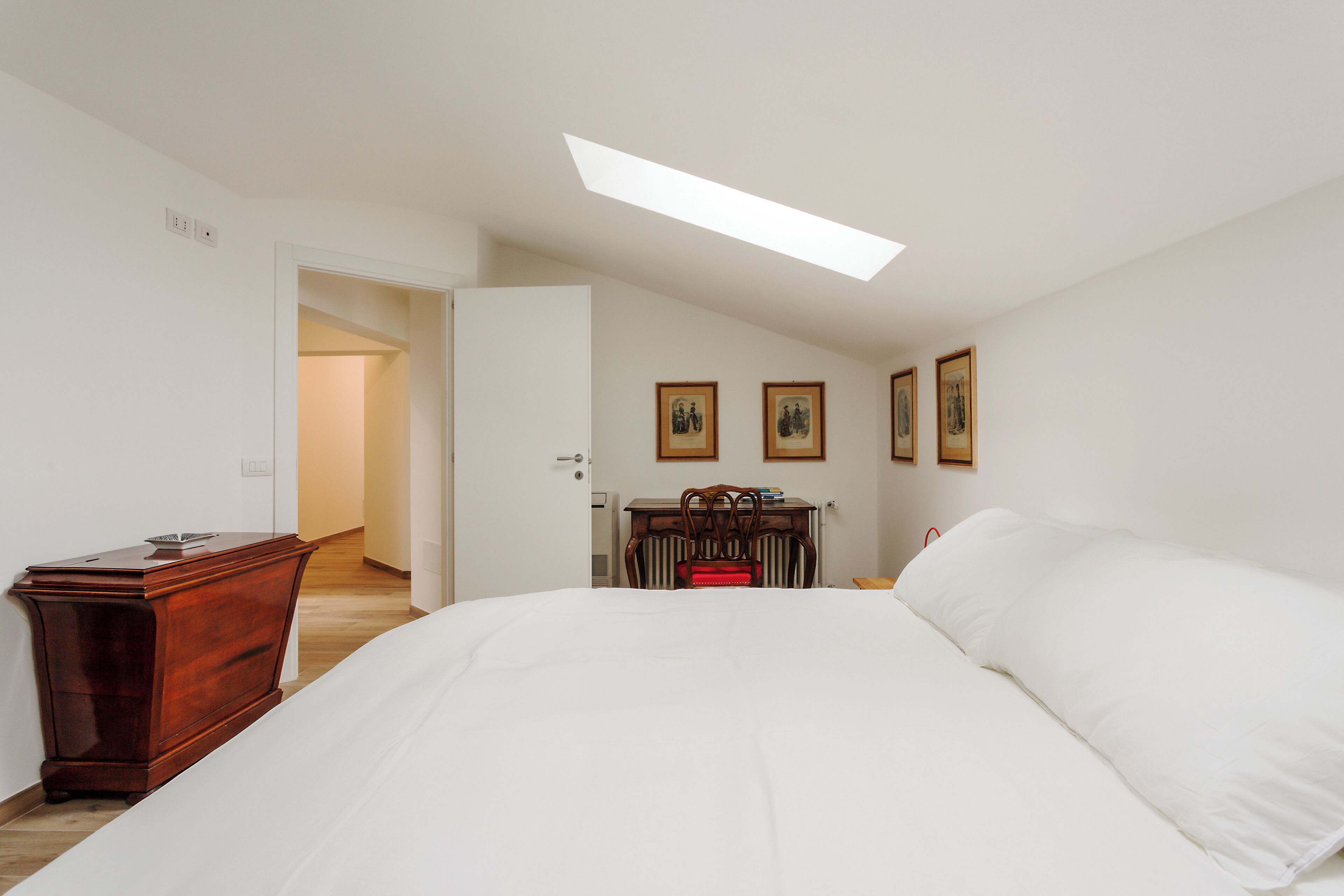 A bedroom with a large bed, a wooden dresser, a desk with a chair, and framed pictures on the wall.