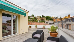 A rooftop terrace with wicker furniture, potted plants, and a view of surrounding buildings. - Amazing flat with big terrace and private car park (Verona)