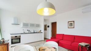 A modern kitchen with white cabinets, a red sofa, and a glass dining table. - Amazing flat with big terrace and private car park (Verona)