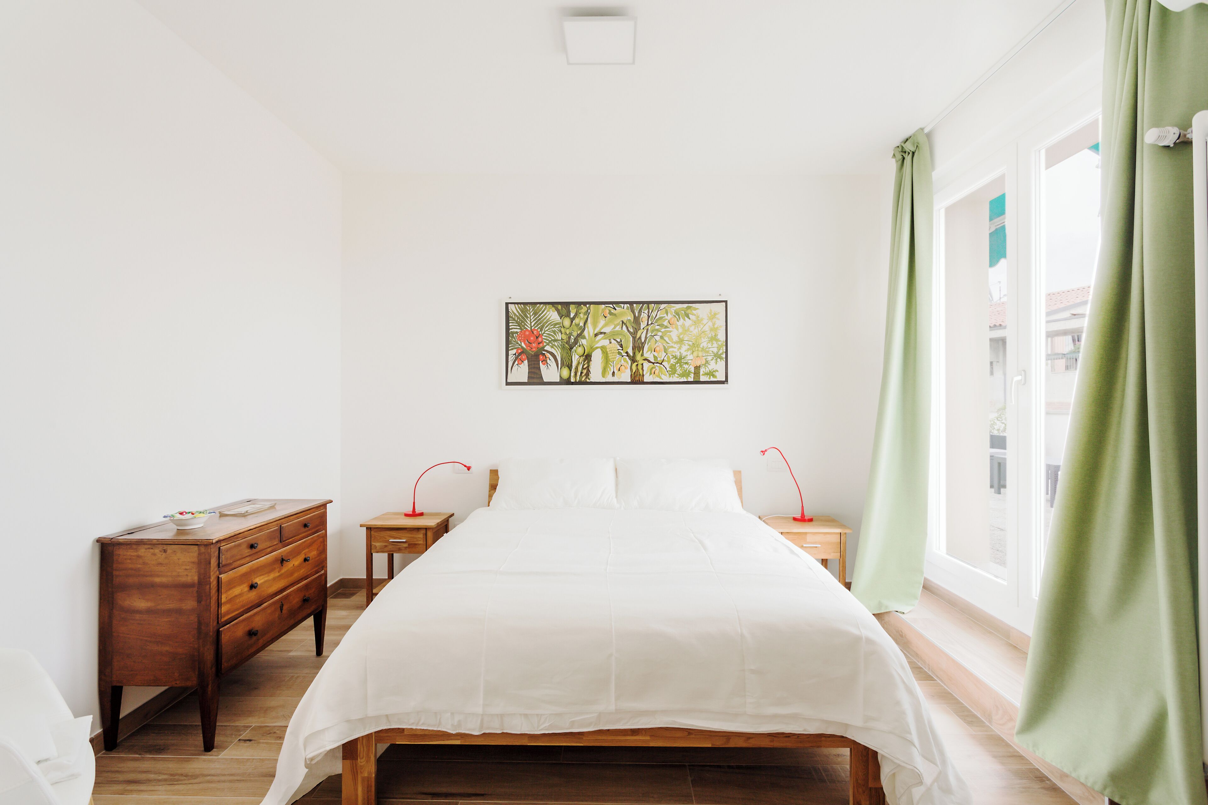 A bedroom with a wooden bed, a nightstand, a dresser, and a window with green curtains.