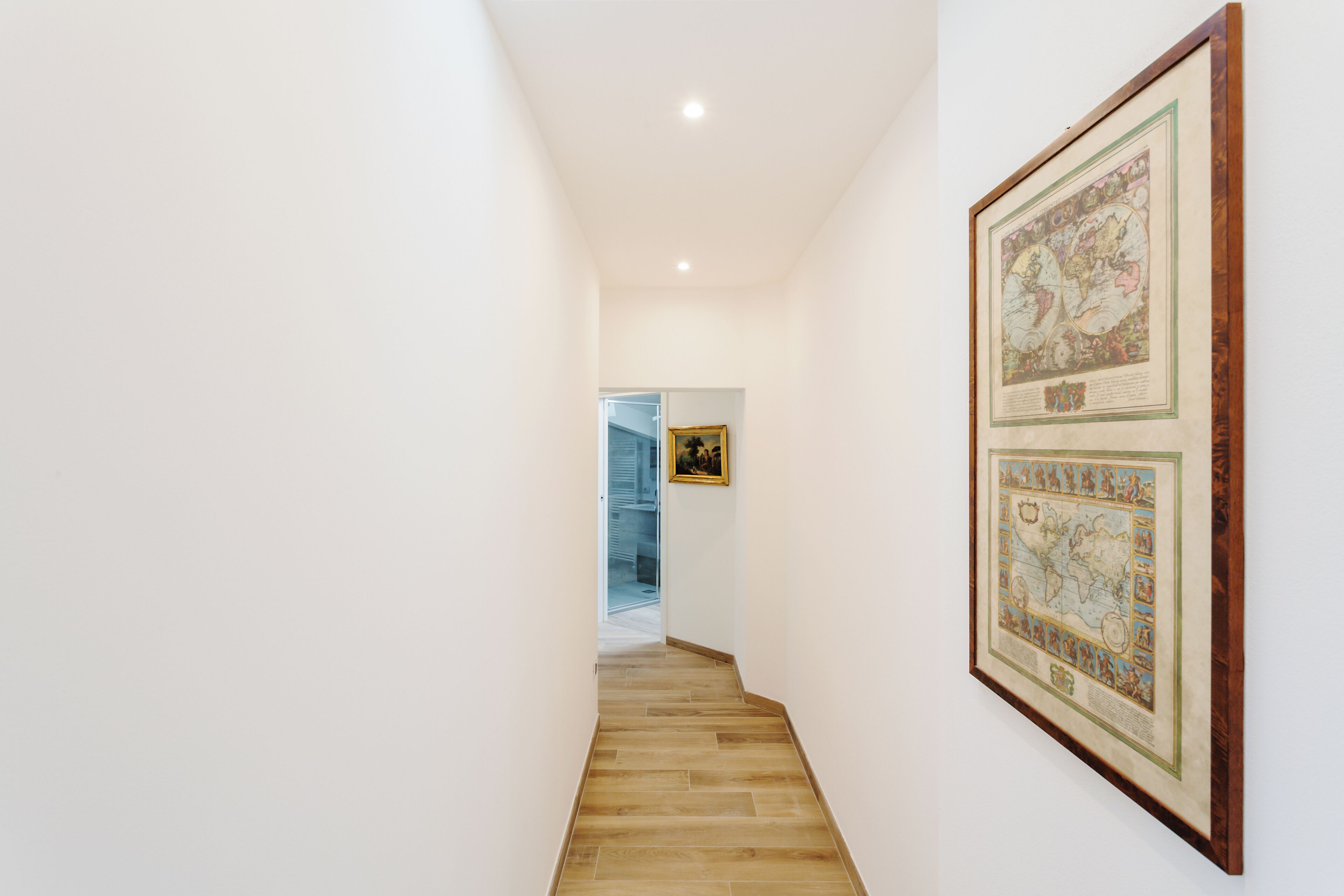 A hallway with a wooden floor and a framed map on the wall.