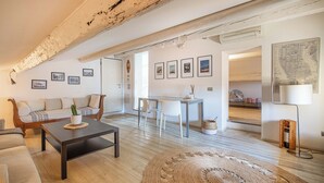 Een ruime woonkamer met houten plafond, een bank, salontafel en een eettafel met stoelen.