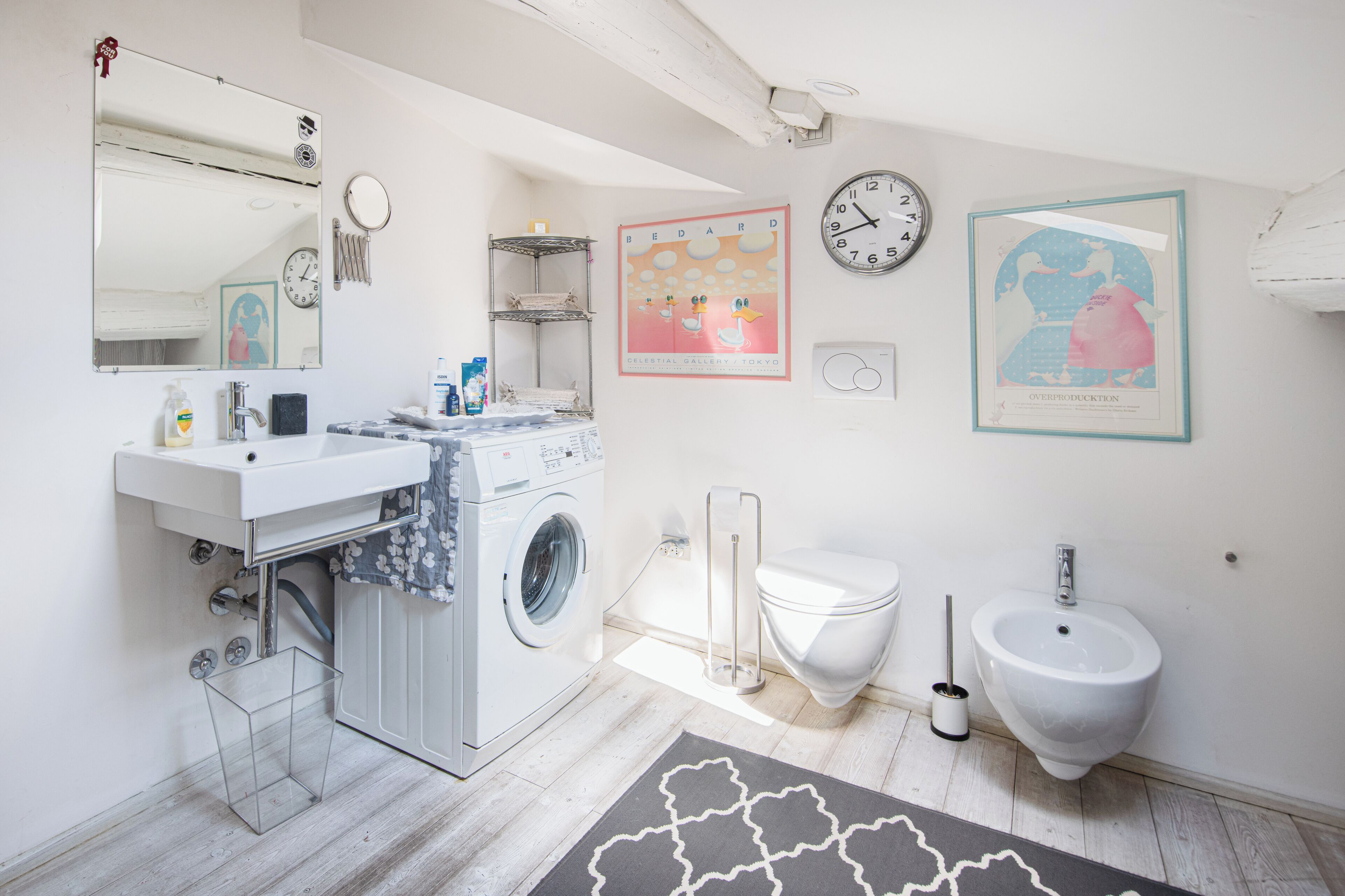 A modern bathroom with a washing machine, sink, toilet, bidet, and decorative wall art.