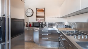Een moderne keuken met roestvrijstalen apparatuur, een magnetron, een koffiezetapparaat en een klok aan de muur.