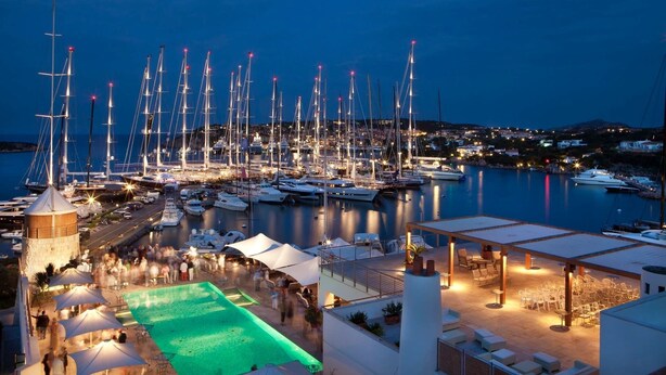 Un port de plaisance au crépuscule, avec de nombreux voiliers amarrés, une piscine et des espaces de détente en plein air.