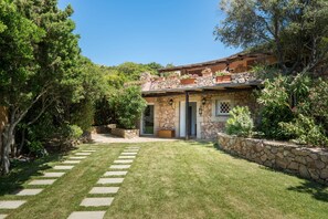 A stone house with a stone pathway leading to the entrance, surrounded by lush greenery and trees. - NEW! Villa Roberta - walk distance to Porto Cervo (Porto Cervo)
