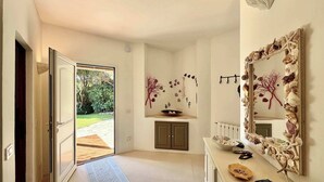 Un intérieur moderne avec une porte donnant sur un espace extérieur, un mur décoratif orné de coquillages et d’un arbre, et un miroir avec un cadre en coquillage.