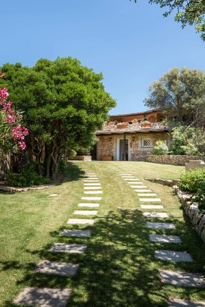 A stone building with a door, surrounded by a well-maintained garden with a stone pathway leading to the entrance. - NEW! Villa Roberta - walk distance to Porto Cervo (Porto Cervo)