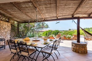A covered outdoor dining area with a stone wall, a table set for four, and a view of greenery and hills. - NEW! Villa Roberta - walk distance to Porto Cervo (Porto Cervo)