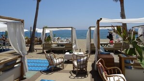 A beachside lounge with outdoor seating, palm trees, and a view of the sea.