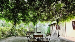 A stone patio with a table and chairs, surrounded by a wrought iron fence and lush greenery. - Beautiful country house in the heart of Tuscany (Capolona)