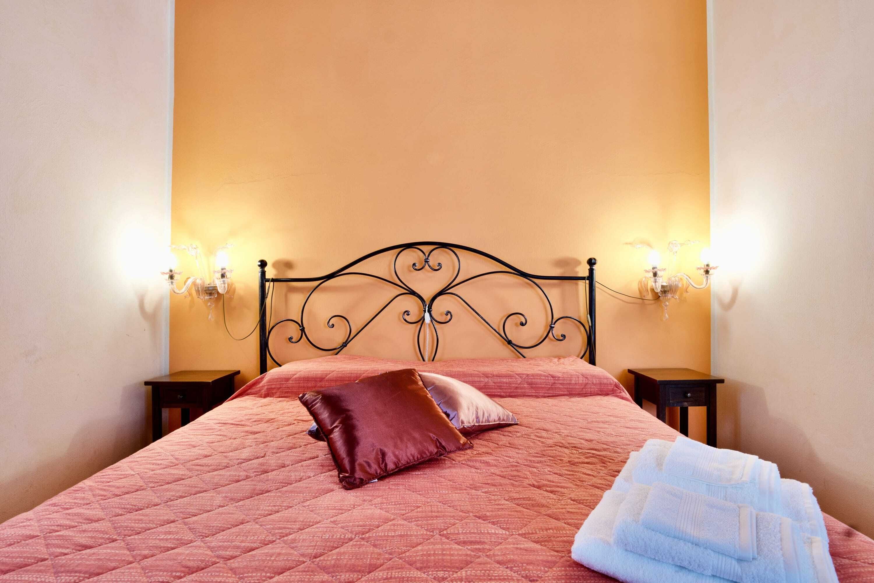 Un lit bien fait, recouvert d’une couette rose, avec deux oreillers et une pile de serviettes blanches.