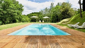 A rectangular swimming pool with a wooden deck, surrounded by lush greenery and two white umbrellas. - Beautiful country house in the heart of Tuscany (Capolona)
