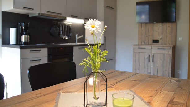 A wooden dining table with a vase of flowers, a glass of water, and a candle.