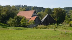 A traditional barn with a red roof and a smaller adjacent building with a gabled roof, surrounded by lush greenery and trees.