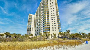 A high-rise hotel with multiple balconies, located near a beach with sandy dunes and palm trees. - Remodeled, Open Airy Condo, With Full Access , 1706 Brighton 3 Bedroom Condo (Myrtle Beach)