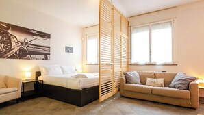 Une chambre moderne avec un lit, des tables de chevet, un canapé et une grande fenêtre.