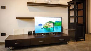 Un salon moderne avec un téléviseur à écran plat posé sur un meuble TV en bois foncé, une petite étagère au-dessus du téléviseur et un buffet en bois foncé sur le côté droit.