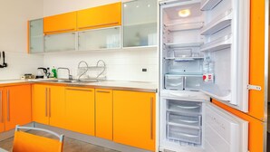 Une cuisine avec des meubles de couleur orange, un réfrigérateur blanc et un évier avec un robinet.
