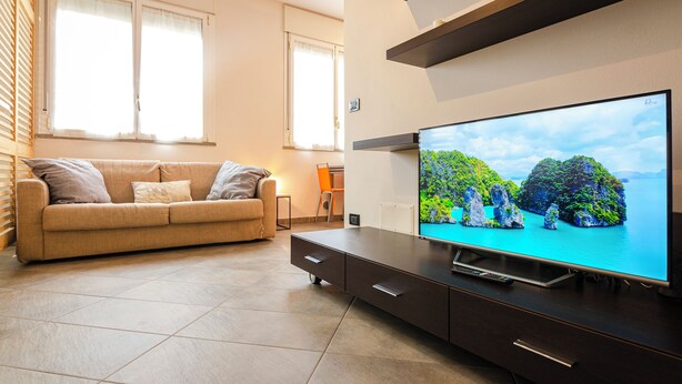 Un salon moderne avec un canapé, un téléviseur et une vue sur une île tropicale.