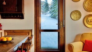 A wooden dining table with a bowl of oranges, a wooden cabinet, and a window with a snowy view. - Cozy flat with direct access to garden (Cortina d'Ampezzo)