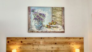 A bedroom with a wooden headboard, two bedside lamps, a bed with white linens, and a painting of flowers on the wall. - Cozy flat with direct access to garden (Cortina d'Ampezzo)