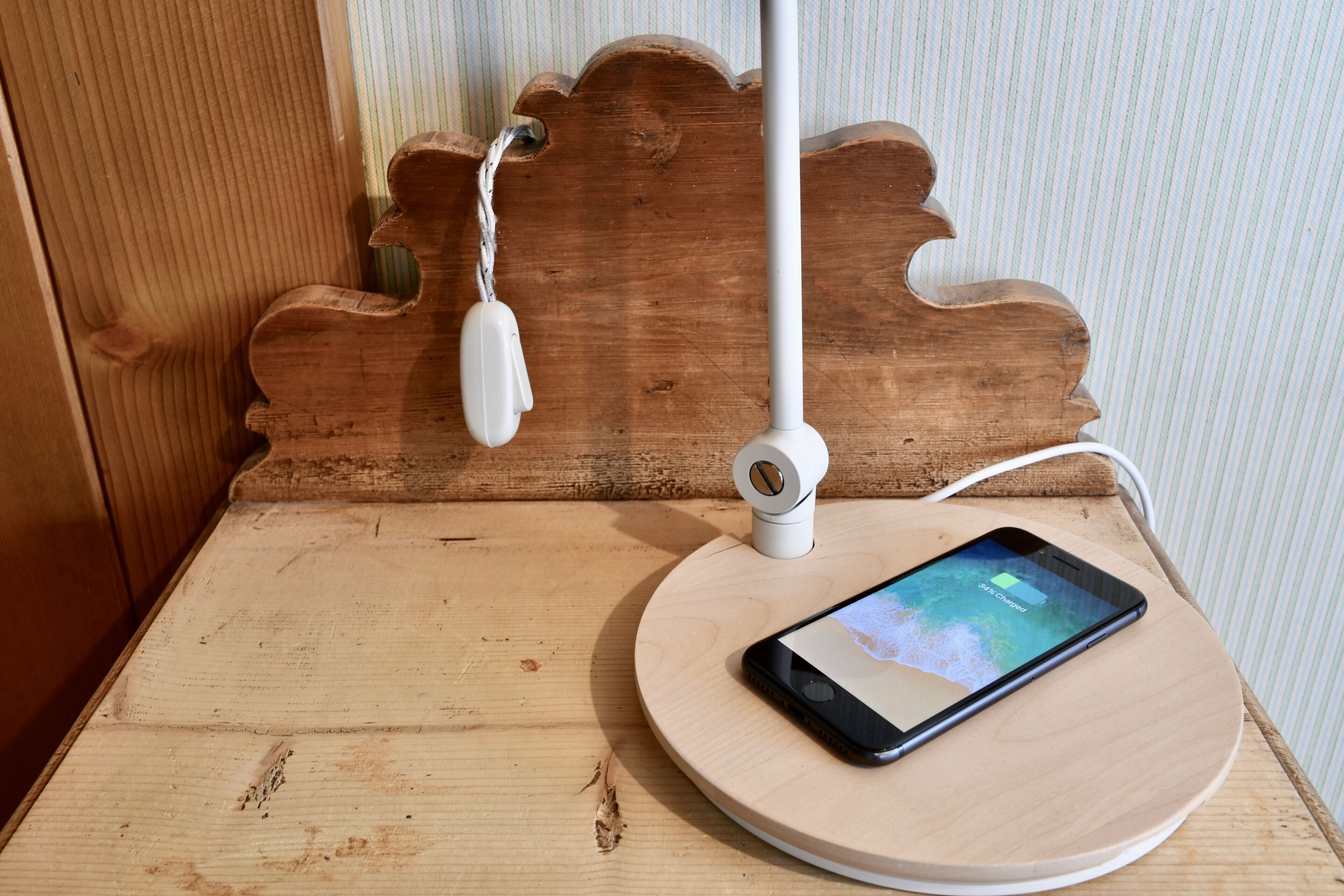 Un teléfono inteligente sobre un soporte de madera para cargarlo, con una lámpara blanca a un lado.