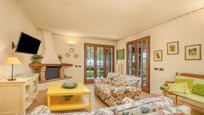 A living room with a sofa, a coffee table, a TV, and a fireplace. - Beautiful villa with private garden and pool (Costermano)