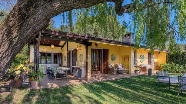 A yellow house with a patio, outdoor seating, and a large tree. - Beautiful villa with private garden and pool (Costermano)
