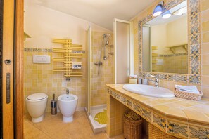Bathroom features a toilet, bidet, and shower area with a glass door, along with a large mirror and wicker storage.