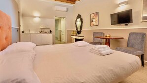 A hotel room with a large bed, a small table with a chair, a TV mounted on the wall, and a kitchenette in the background. - Palazzo Cavalli - Deco' (Verona)