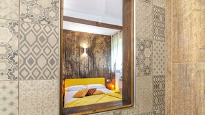 Un dormitorio con cama, mesita de noche, lámpara y espejo.