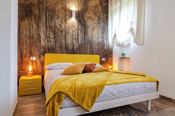 Une chambre à coucher avec un lit, des tables de chevet jaunes et un mur orné d’un motif texturé.