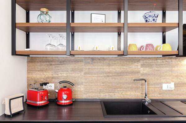 Una cocina con protector de madera, un lavamanos negro y dos hervidores rojos sobre la encimera.